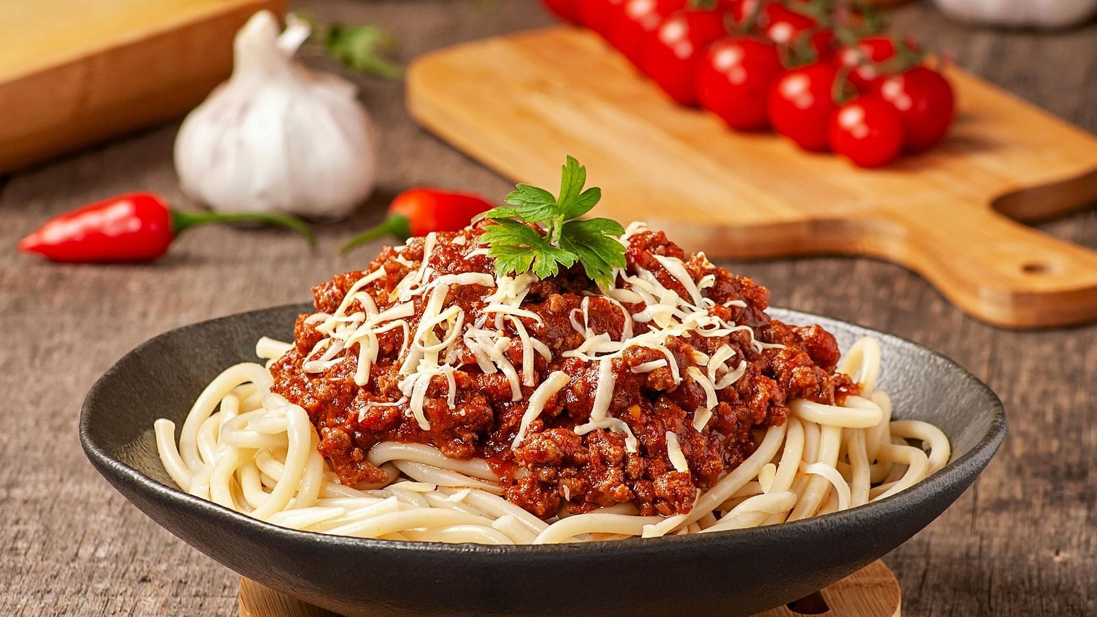 a bowl of spaghetti served with a meaty red sauce with grated cheese topped with basil leaves
