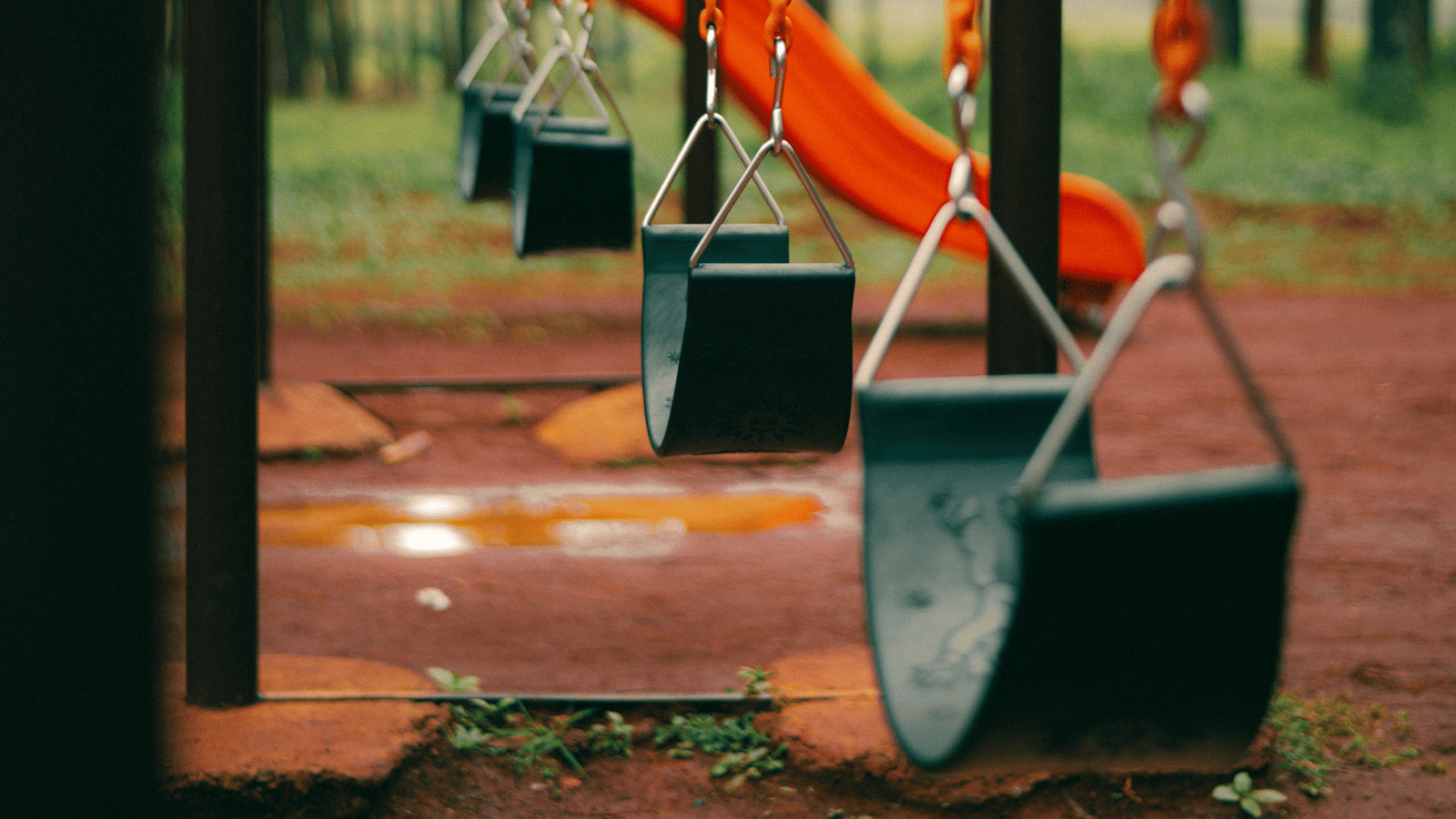 A green and orange swingset in a park.