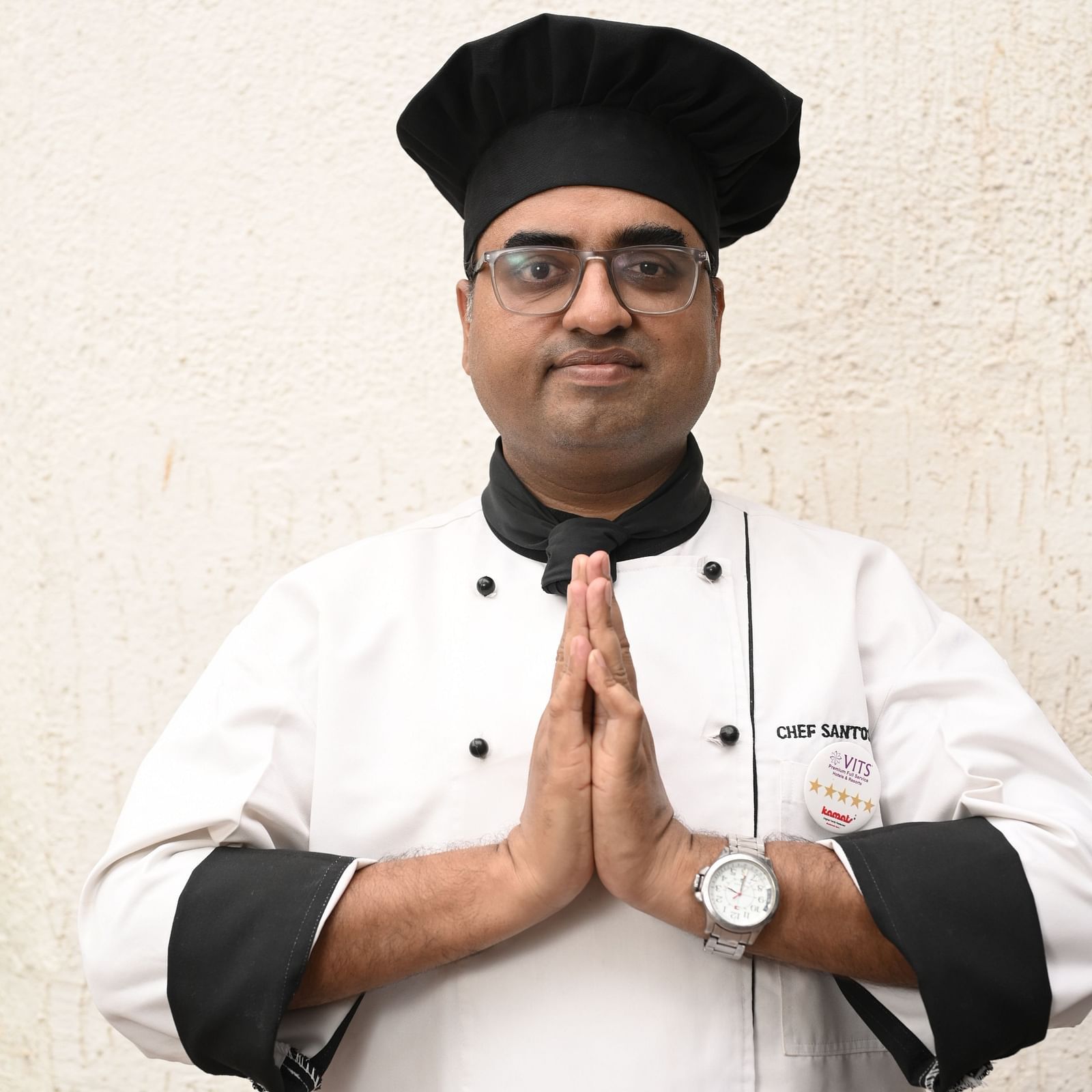 Chef in uniform greeting with folded hands outdoors - Kamats India