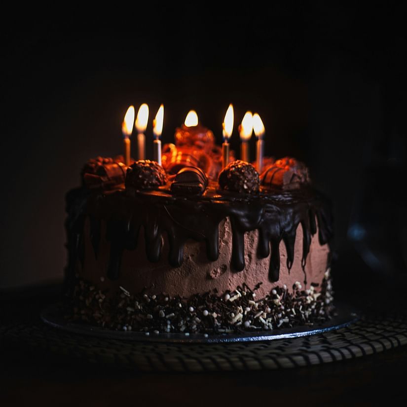 a birthday cake kept on a table with candles lit and a dark background