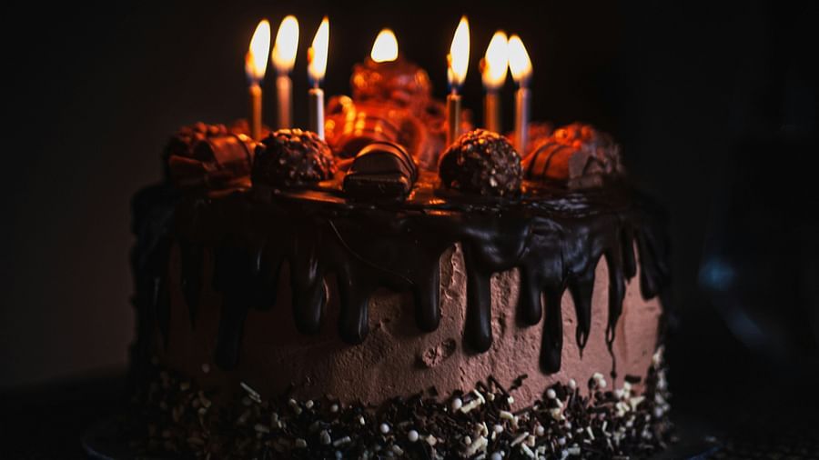 a birthday cake kept on a table with candles lit and a dark background