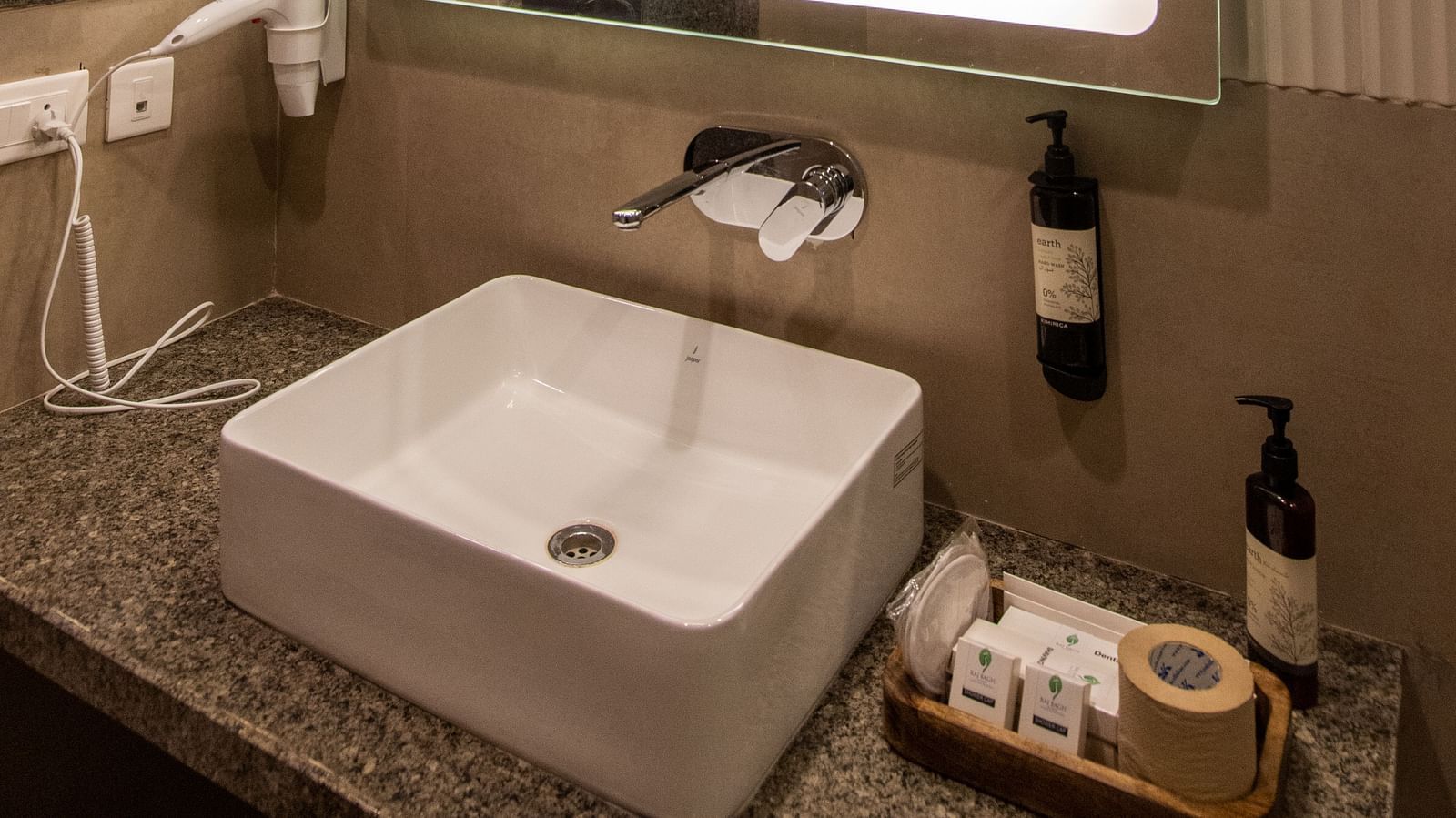 A vanity counter with a sink, a wall-mounted mirror and toiletries - Rajbagh Wellness, Udaipur