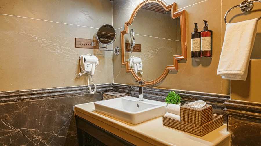 The claasic room bathroom at BluSalzz Terrah Hills Resort, Dalhousie, with a stone sink counter, a round mirror, and a wooden ceiling, designed in a rustic style.