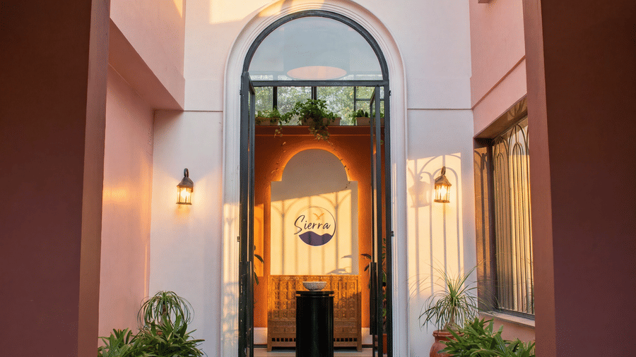 An open arched doorway at The Sierra - By The Lake reveals a stone pathway leading into an illuminated interior courtyard with decorative hanging lamps.