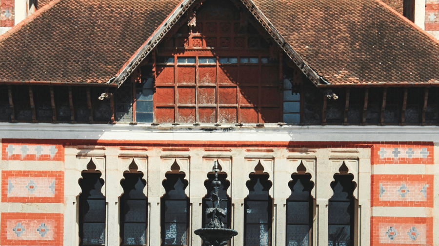 A tall, ornate historic building with a pointed roof, patterned walls, arched windows, and detailed architectural design.