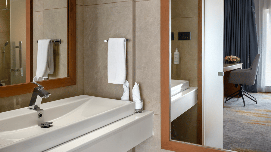 A sleek bathroom layout featuring a white wash basin console, large mirrors, and a view into the bedroom area at Tiara by MPS.