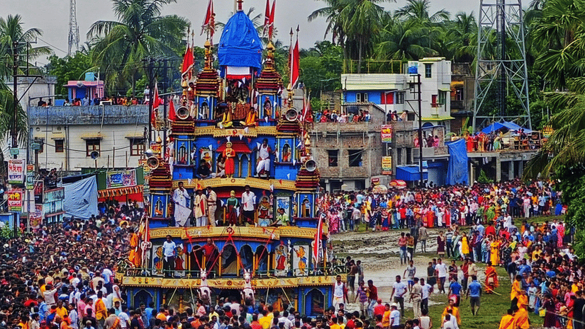 A large wooden chariot with a tall fabric canopy is surrounded by a massive crowd of people in an outdoor setting.