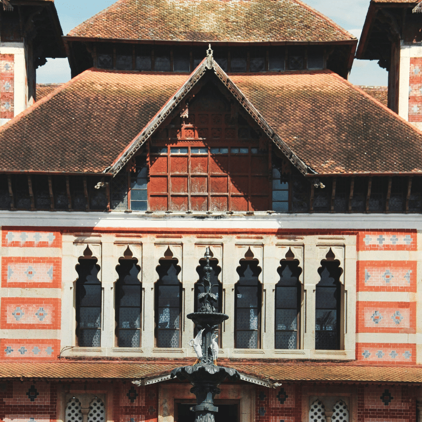 A tall, ornate historic building with a pointed roof, patterned walls, arched windows, and detailed architectural design.