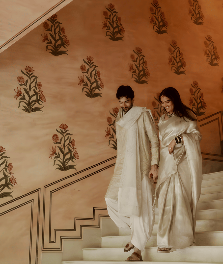 Charvi & Dhruv walking down staircase at Umaid Palace with pastel walls and traditional decor during wedding celebration.