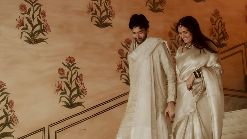 Charvi & Dhruv walking down staircase at Umaid Palace with pastel walls and traditional decor during wedding celebration.