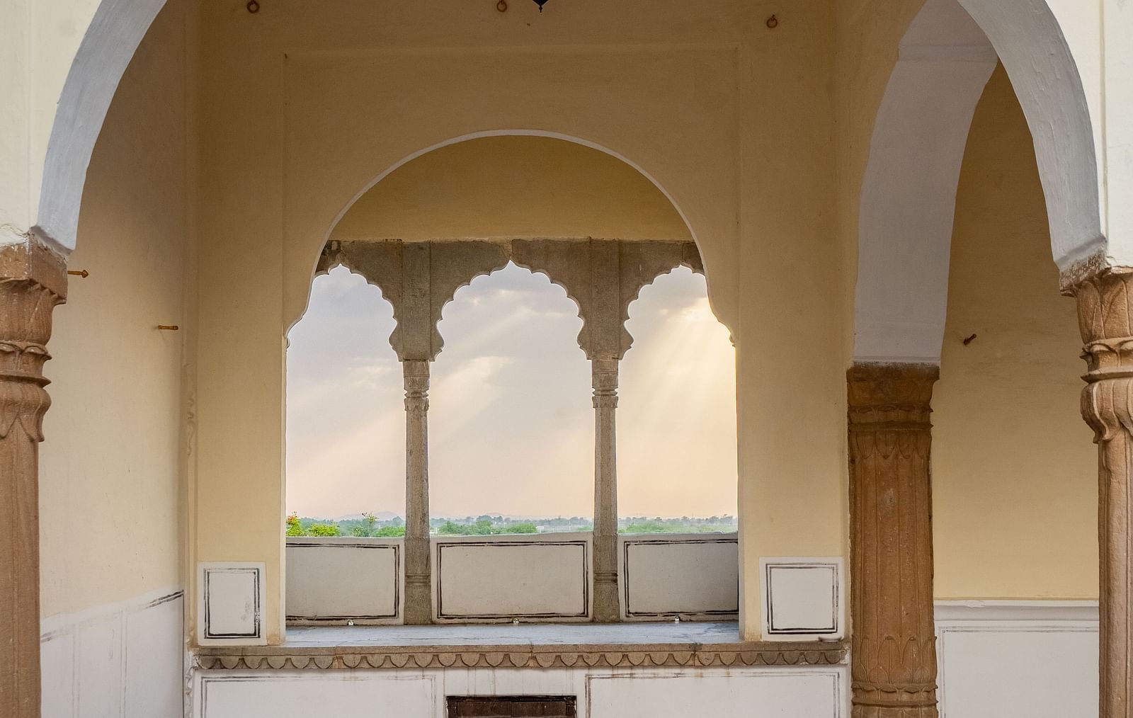 Arched openings reveal a checkered floor and distant view at Fort Barli, Ajmer. A hanging lamp is visible.