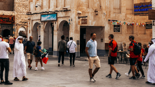 People walking on a paved road in a market with a building in the backdrop