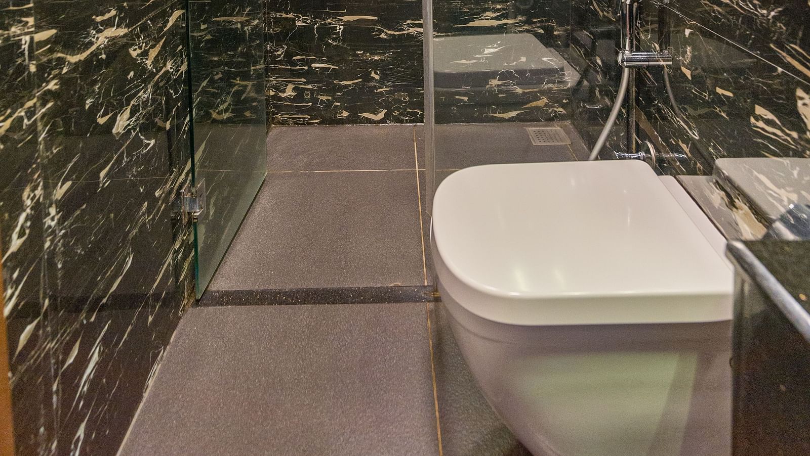 Image of a washroom with a toilet and a shower area in the corner at Hotel Altitude, Madikeri.