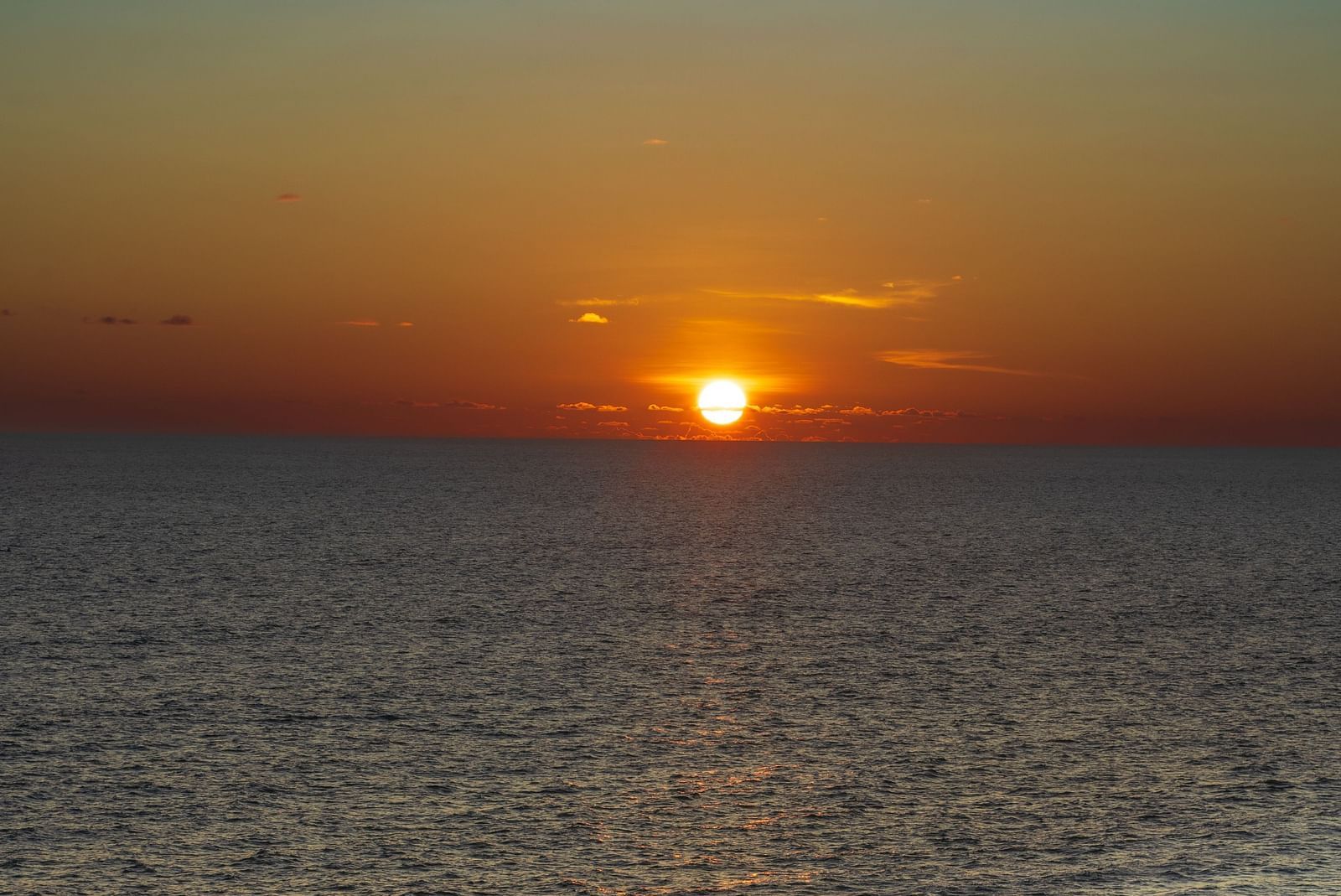 A far out view of Varkala Beach with many people on the shoreline and the sun setting in the background.