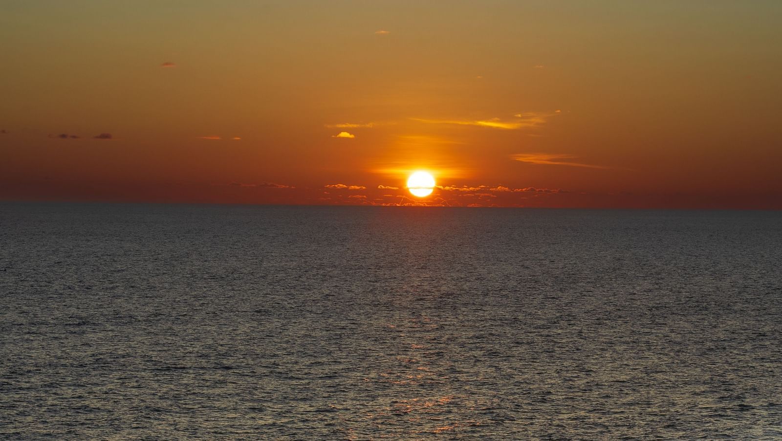An overview of a beach in Varkala with many people on the shores and the sun setting in the background.