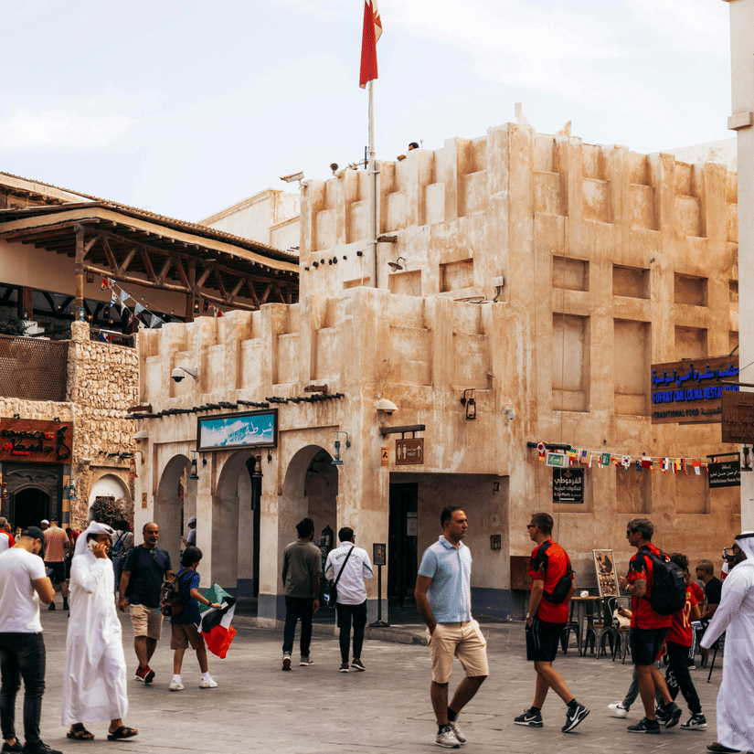 An overview of the Souq Waqif in the distance with people walking in the foreground on the road. It is the best place for travellers to buy unique gifts from Qatar.