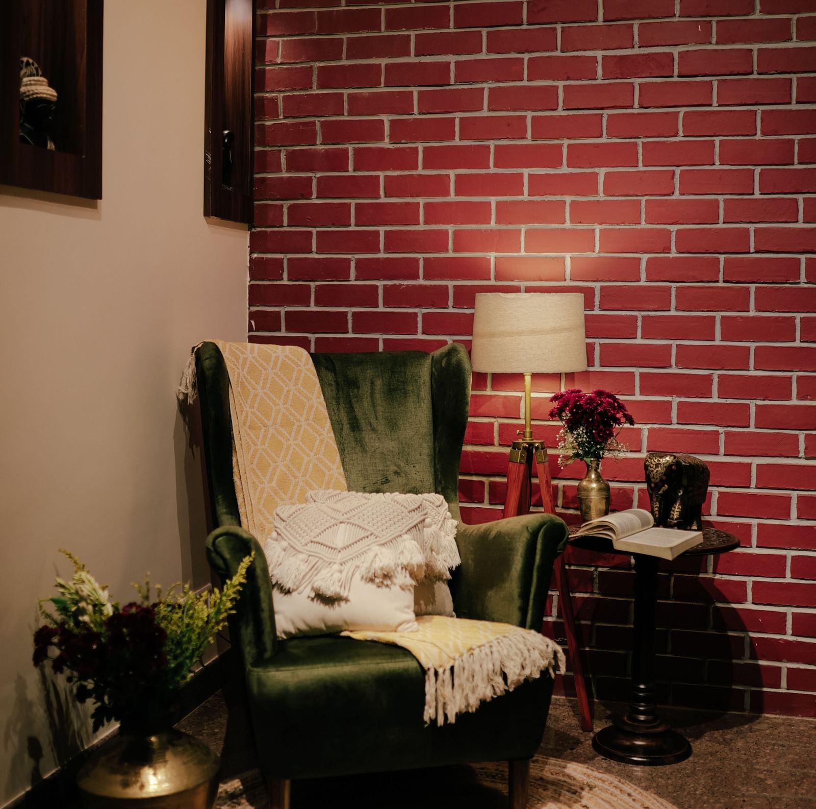 A cosy corner with a green armchair, a small table with a lamp, and a brick wall backdrop | Adhyaya Heritage Reverbed