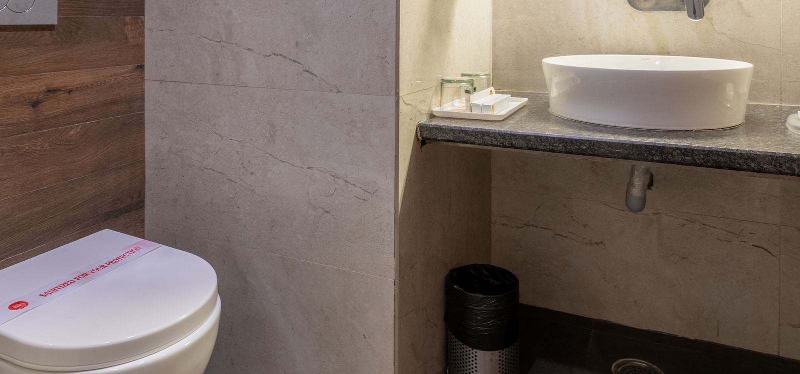 A toilet and washbasin with mirror in a tiled bathroom at Hotel Highway King, Jaipur.