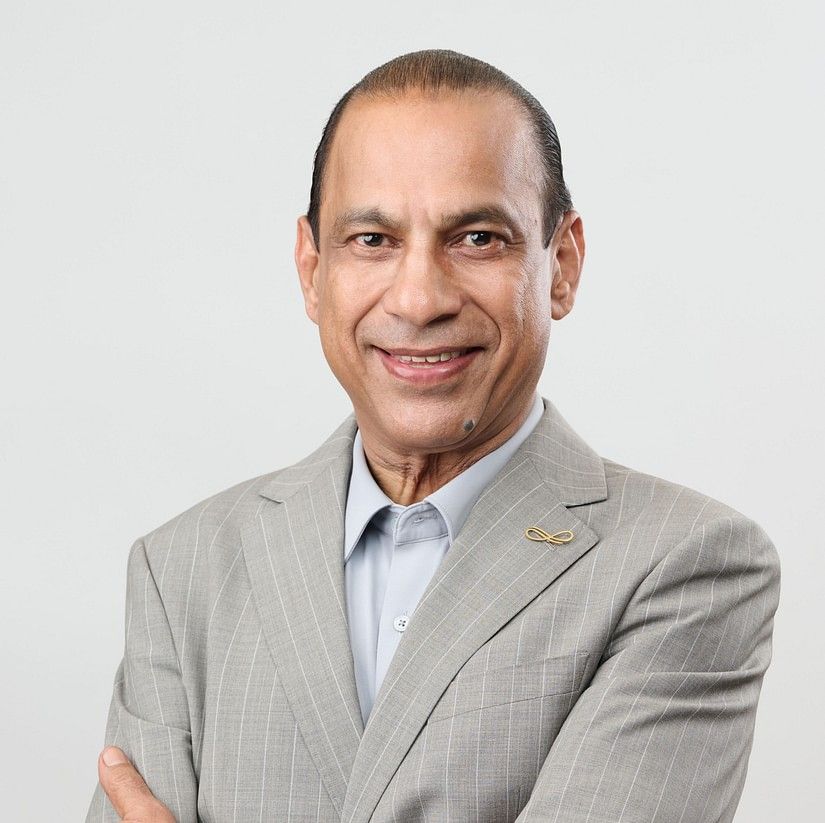 ARUN JAIE in a grey suit, stands with arms crossed, exuding confidence.