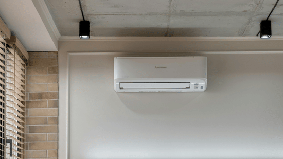 A living area with a sofa, multiple cushions and a wall-mounted air conditioning.