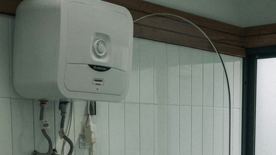 A tiled utility space with a toilet and a large water heater mounted prominently on the wall.