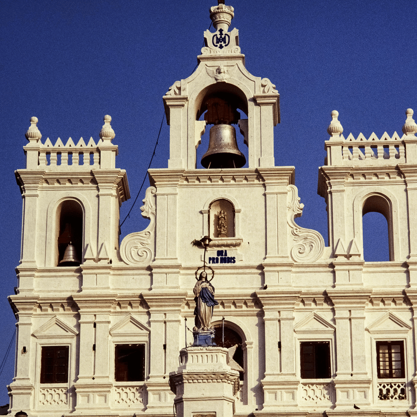 The stunning white facade and bell tower of Se Cathedral in Old Goa, featuring intricate colonial Portuguese architecture.