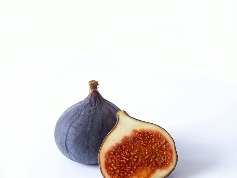 A whole dark purple fig beside a halved fig showing its red seeded interior
