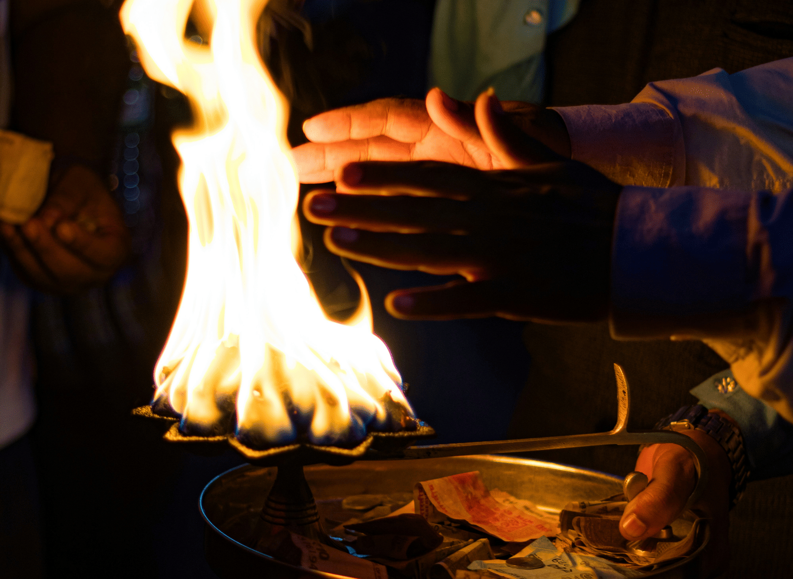 A close-up of a man placing his hands near the aarti thali to receive blessings.