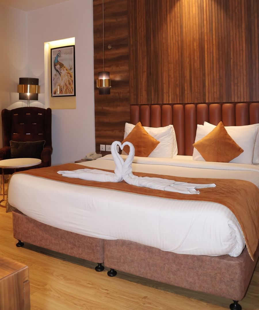 Bedroom with white pillows, wooden panelled wall, bedside lamps and framed artwork at Best Western, Vrindavan.