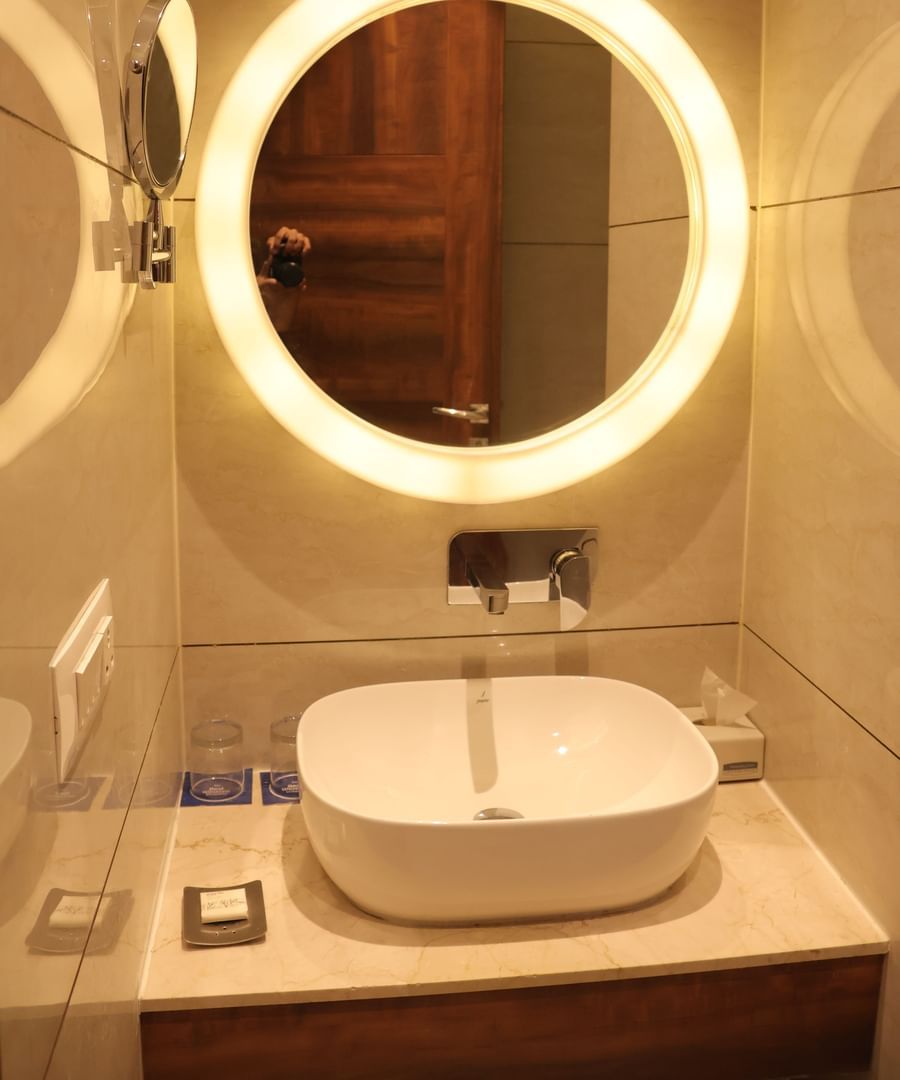 Bathroom vanity with illuminated round mirror, white vessel sink and marble countertop at Best Western, Vrindavan.