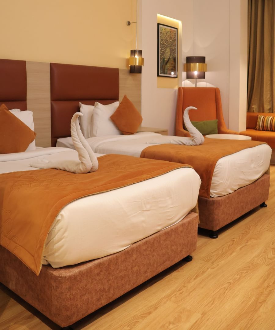 Twin room with orange pillows, wooden headboards, white linens and modern ceiling design at Best Western, Vrindavan.