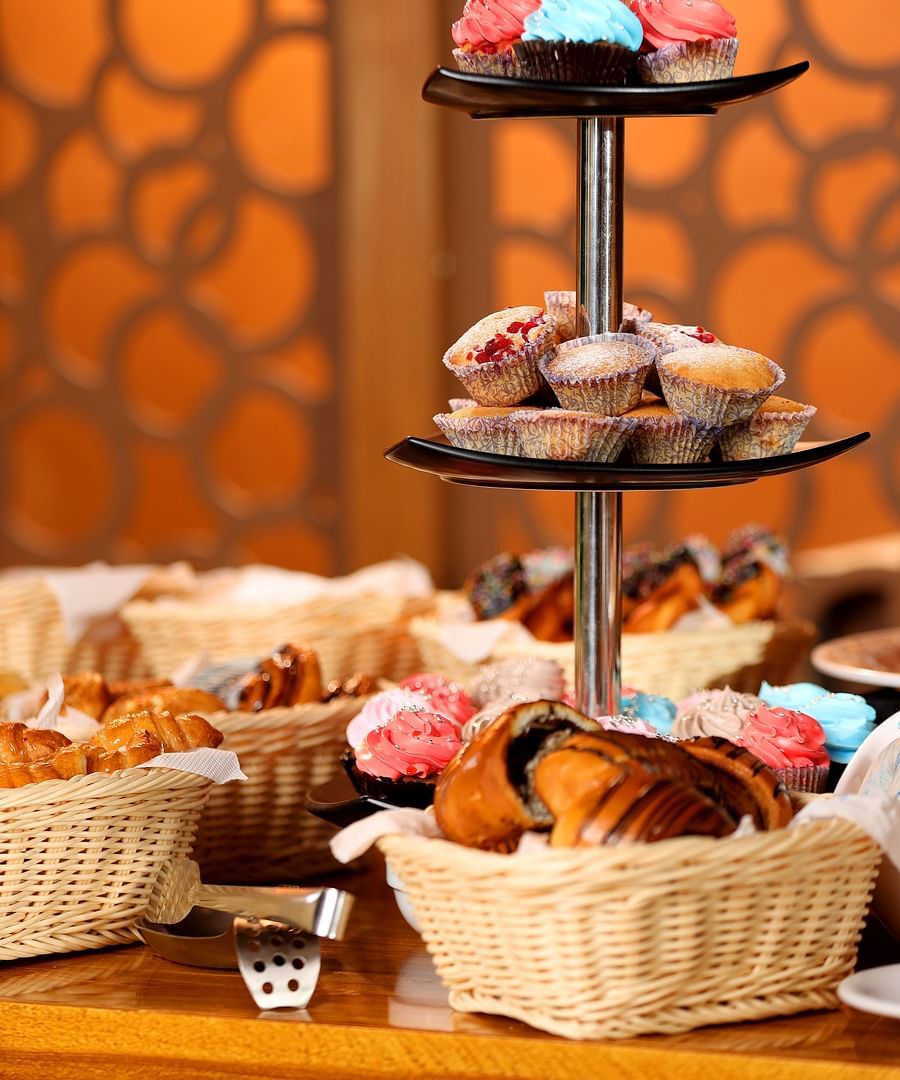 An assortment of muffins, cupcakes, and desserts neatly arranged in baskets on a table at Uday Backwater Resort, with a tong placed beside them