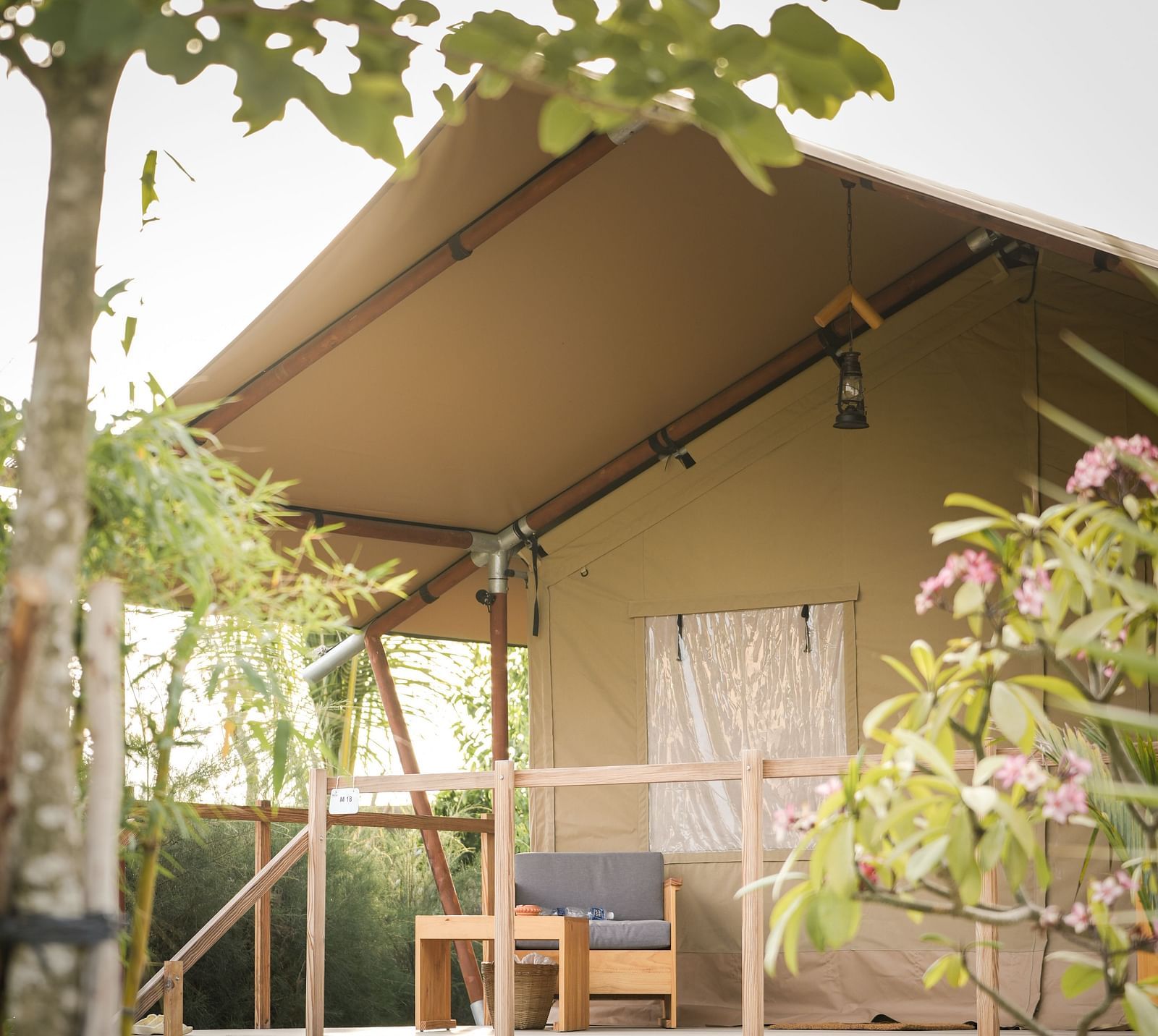 A close-up of the Peaceful Tent at WoCAL Retreat Ke Ga, framed by leafy branches and soft natural light, highlighting a raised wooden structure with a shaded veranda and outdoor seating.