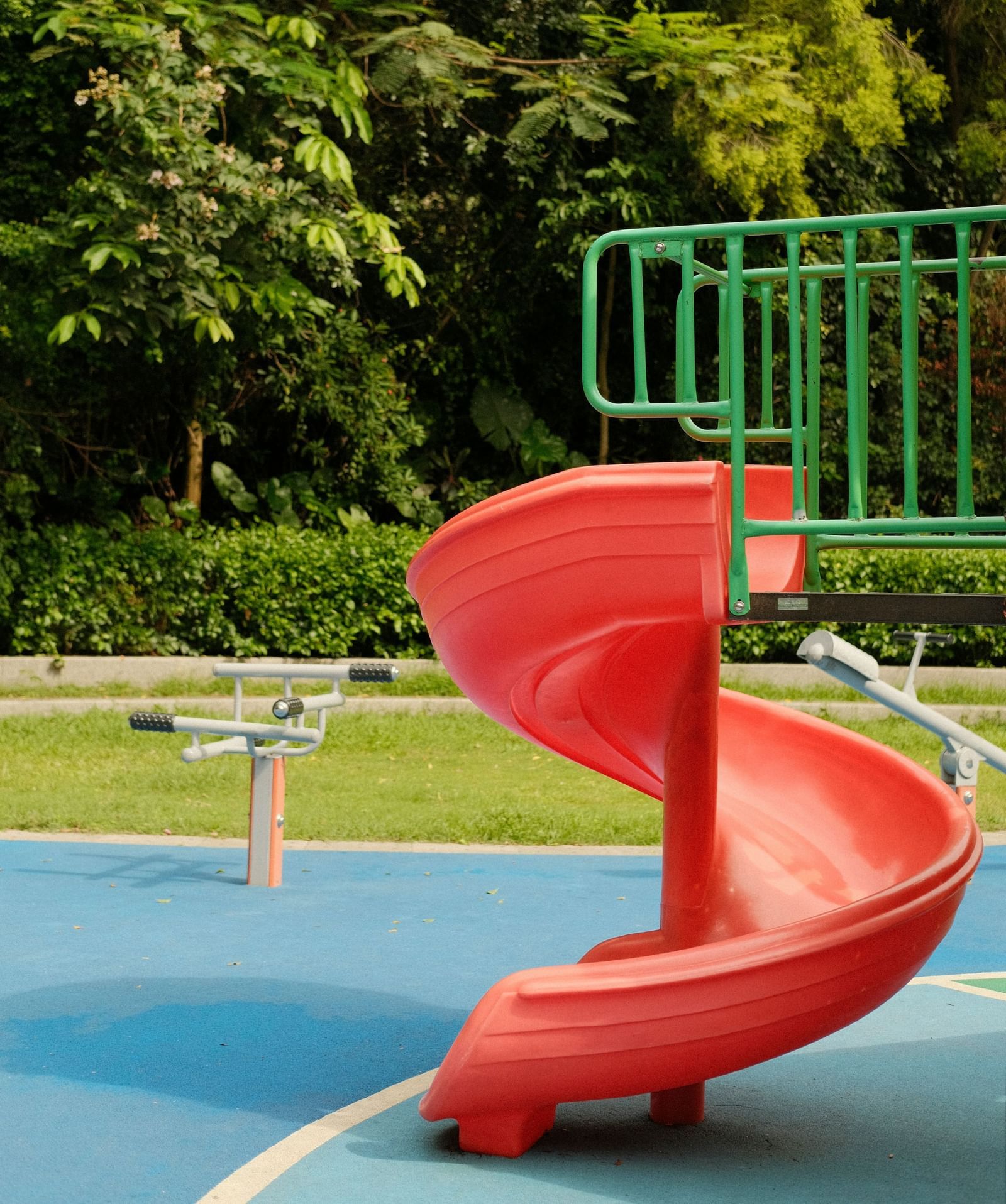 Red spiral slide in an outdoor playground surrounded by greenery.