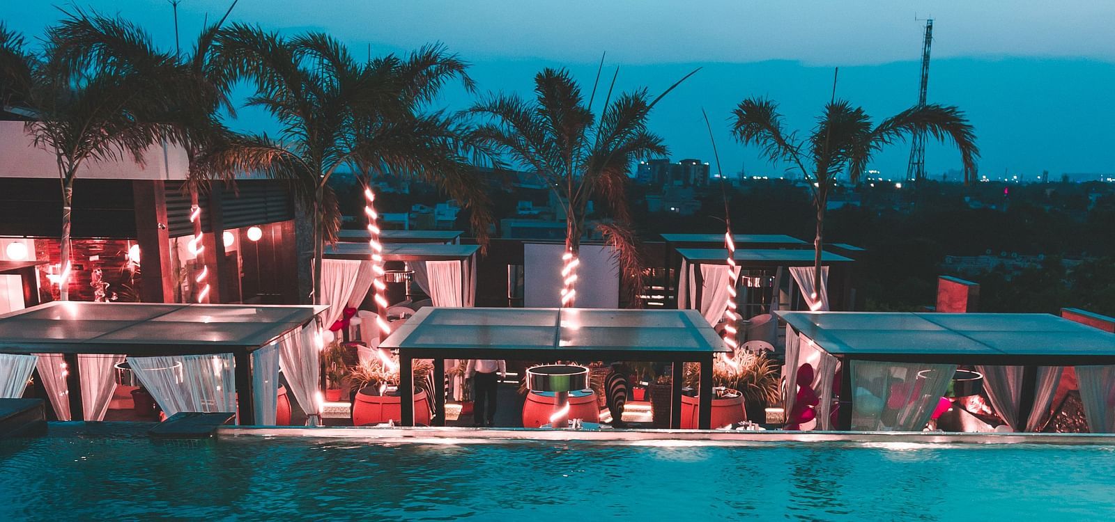 a view of a restaurant with an infinity pool beside and tents kept on the poolside - Hotel Park Elanza, Chennai