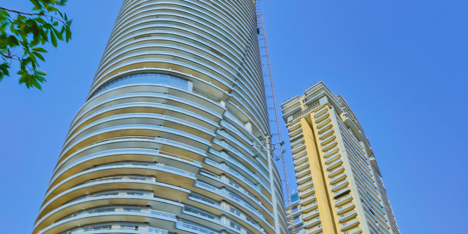 Exterior view of Livbox Supernova, Noida under a bright blue sky with branches of a tree in the corner.