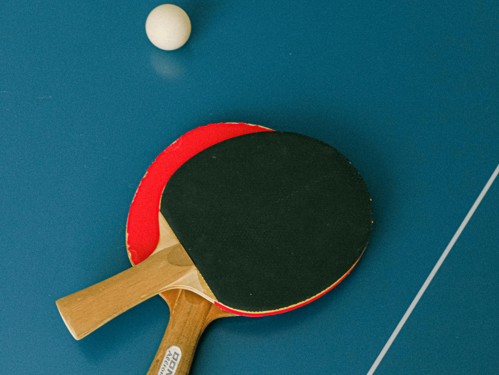 Table tennis paddles and ball placed on a blue playing surface ready for a game.