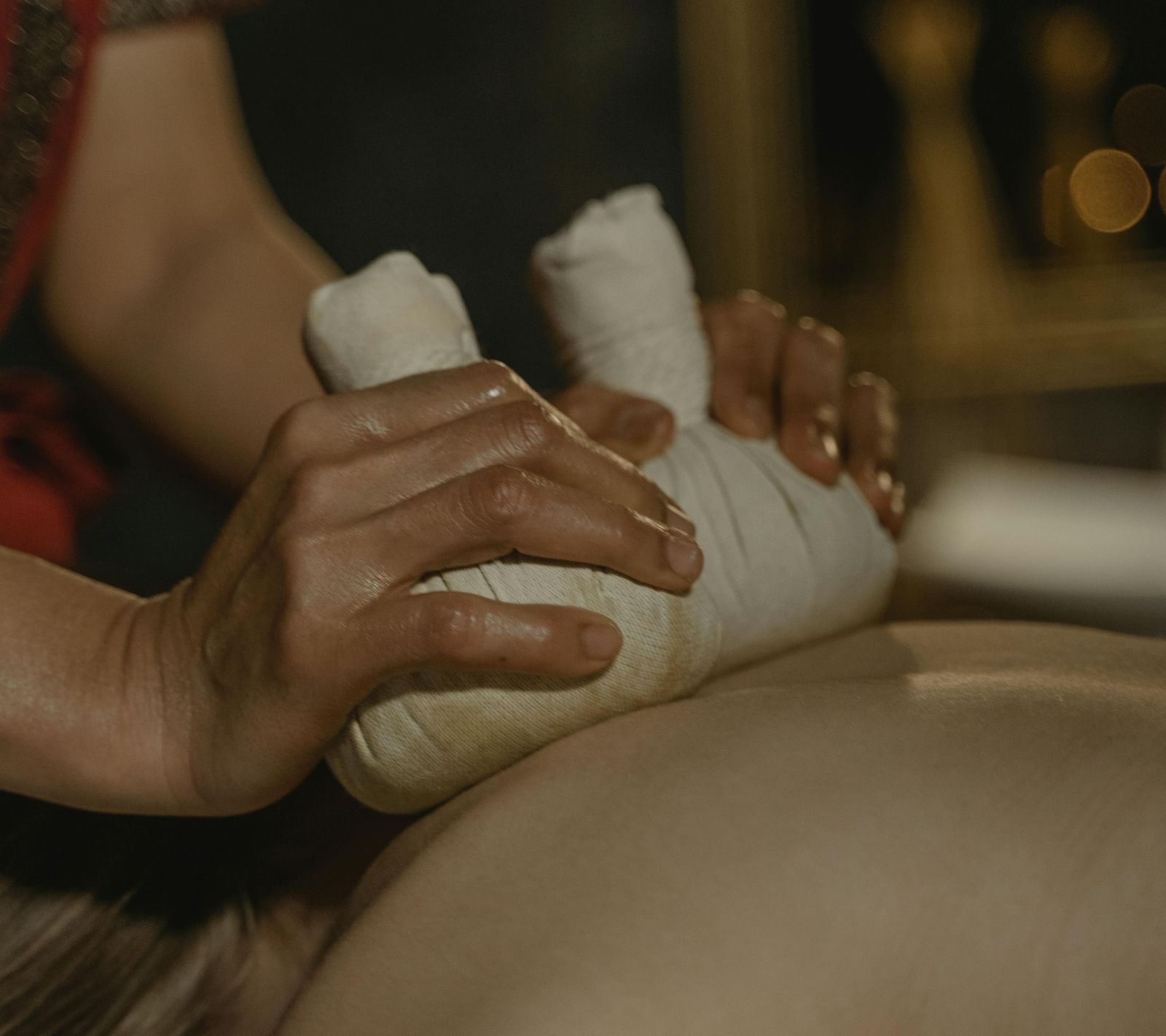 A masseuse using cloth bundles to press the back of a person.