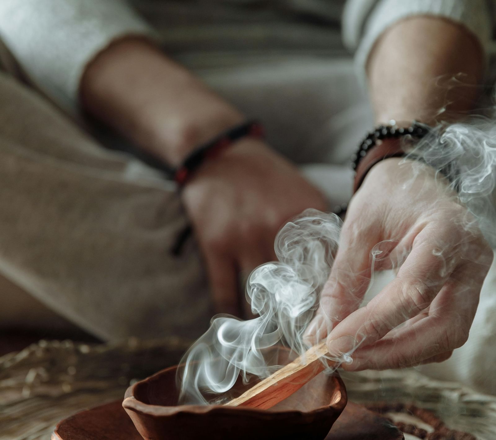 A person sitting on a huge mat burning incense sticks into a bowl.