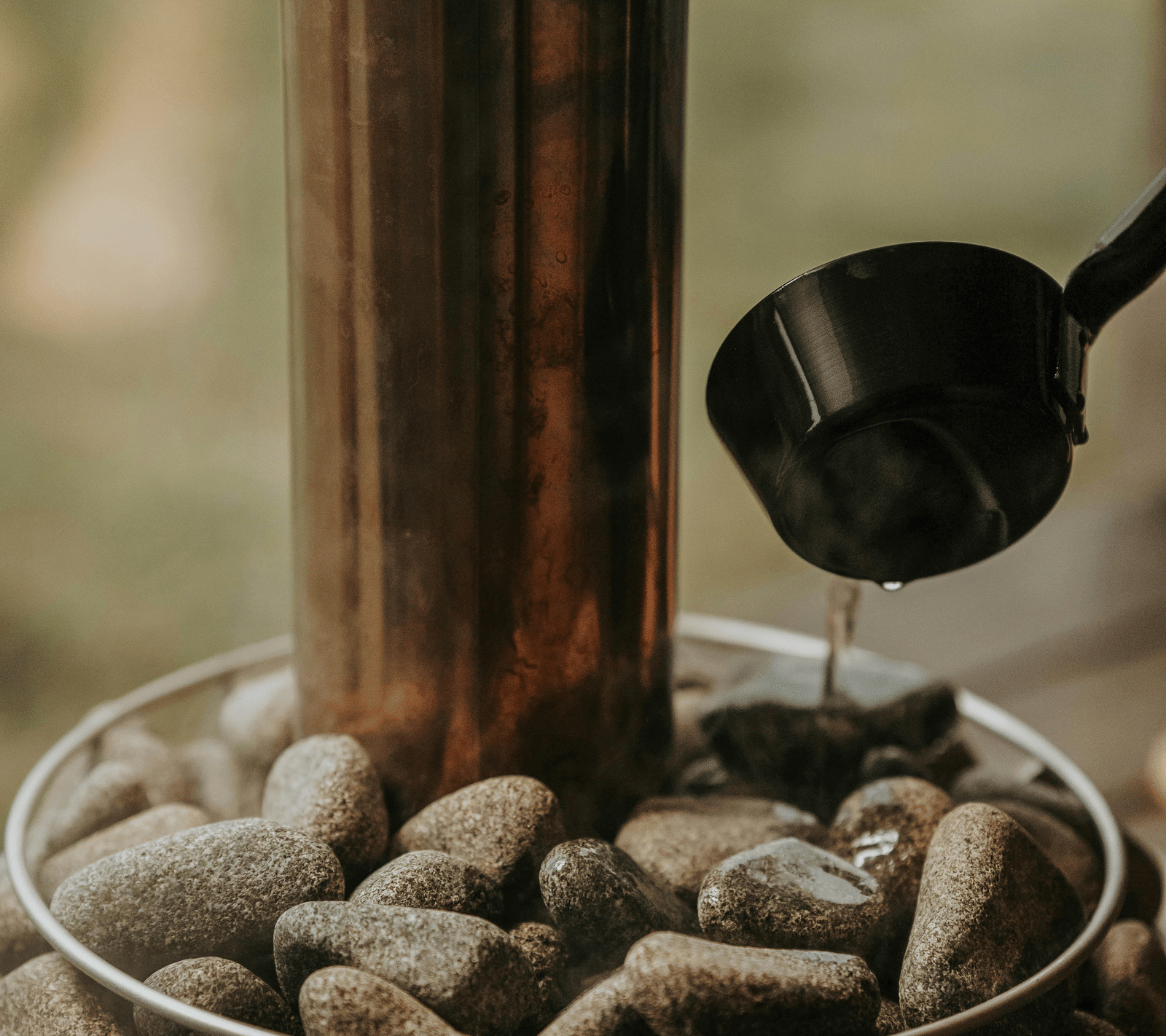 A ladle being used to pour water on hot stones transforming it into steam.