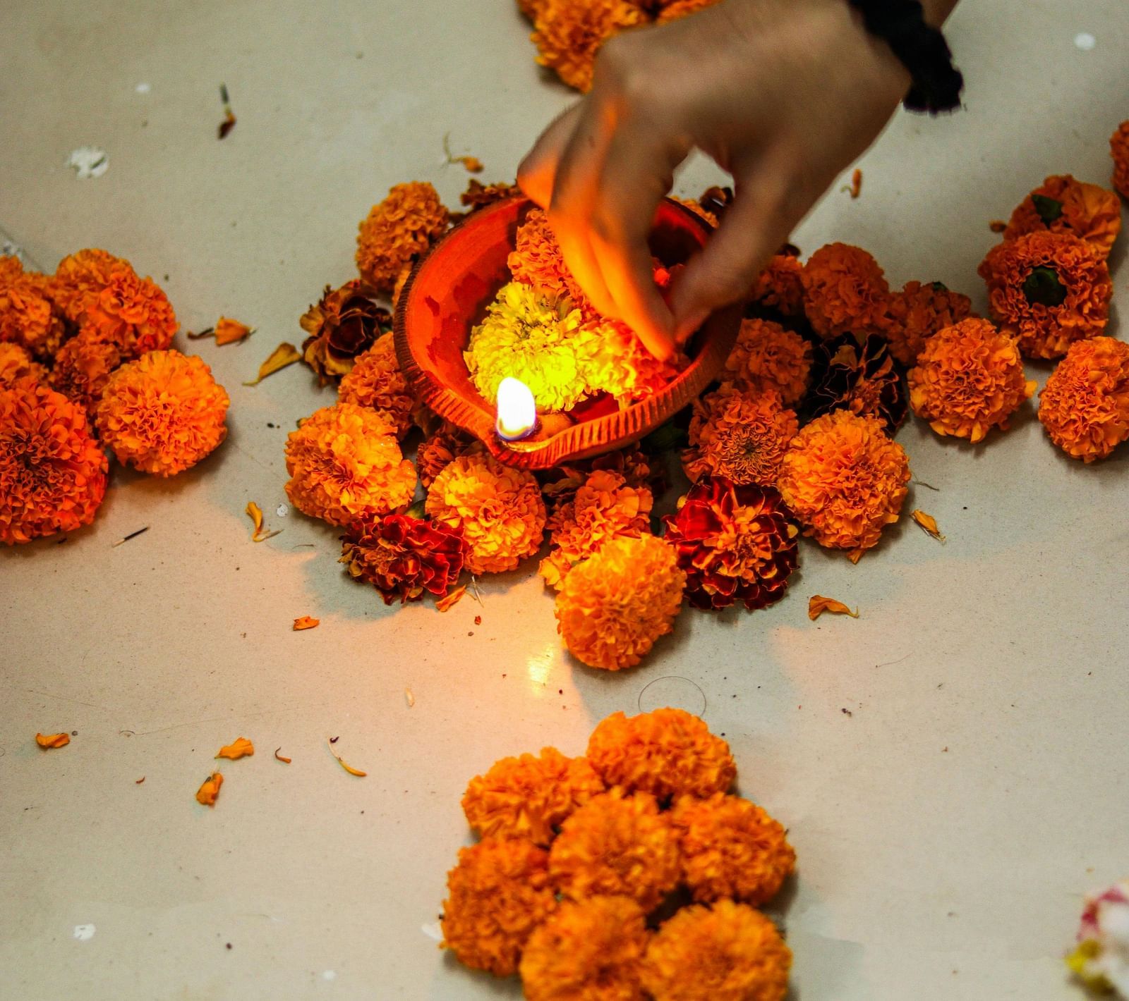 A person placing a flower in the lighted diya.