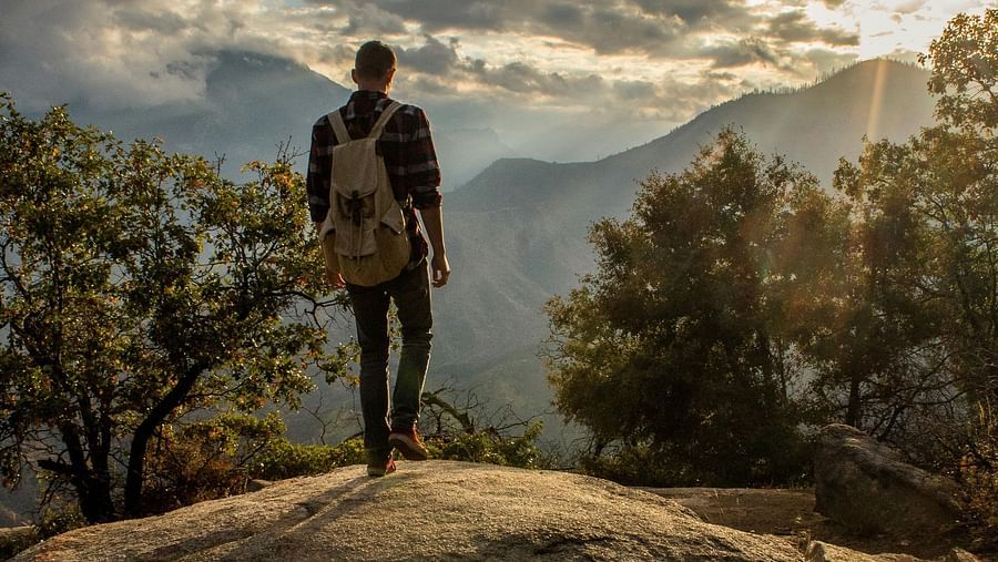 View of a person standing on a cliff watching the sun and the clouds.