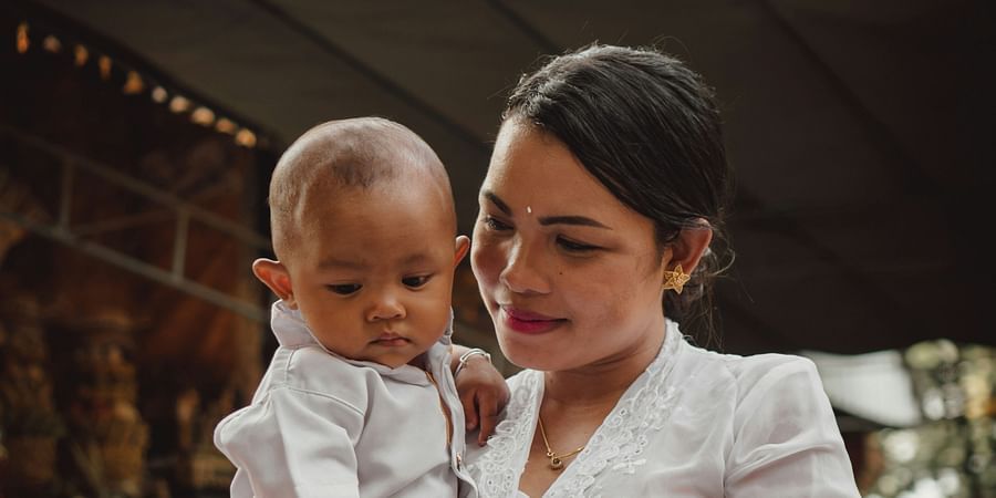 alt-text A mother holding a baby on her waist, both beautifully dressed up in white outfits.