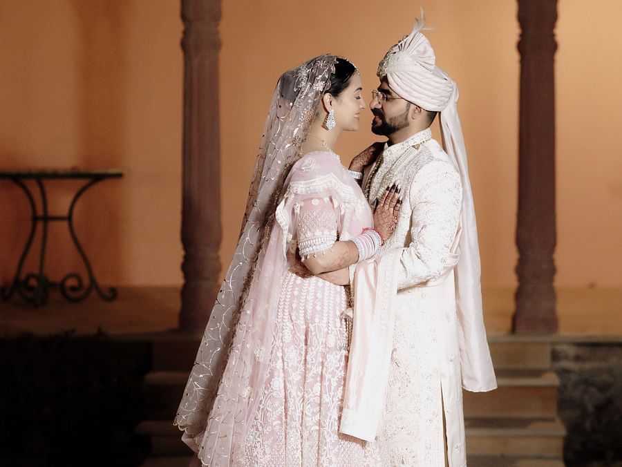 Bride and groom in pastel attire posing in an archway with soft natural lighting.