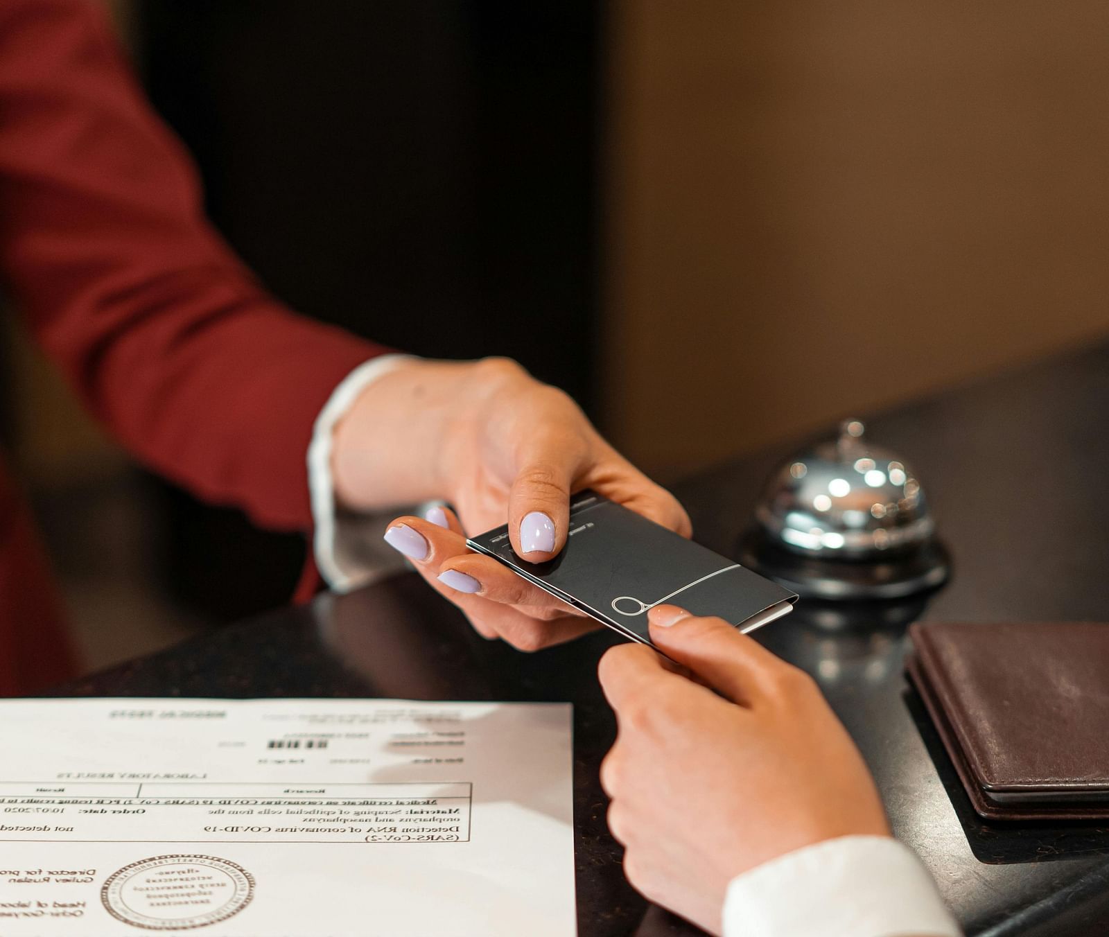 A person behind the reception desk handing over a card to another person with a sheet kept over the desk.