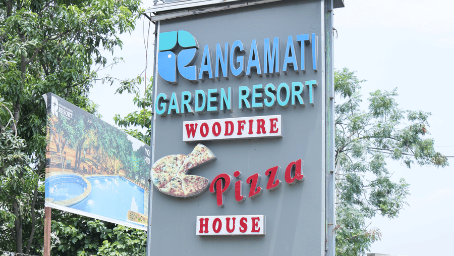 A tall, grey signpost for a resort and pizza outlet standing by the side of a road.
