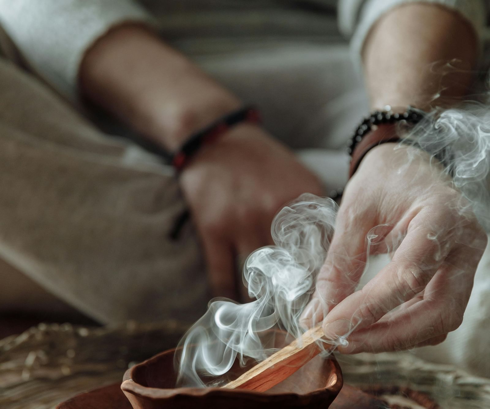 A person sitting on a huge mat burning incense sticks into a bowl.