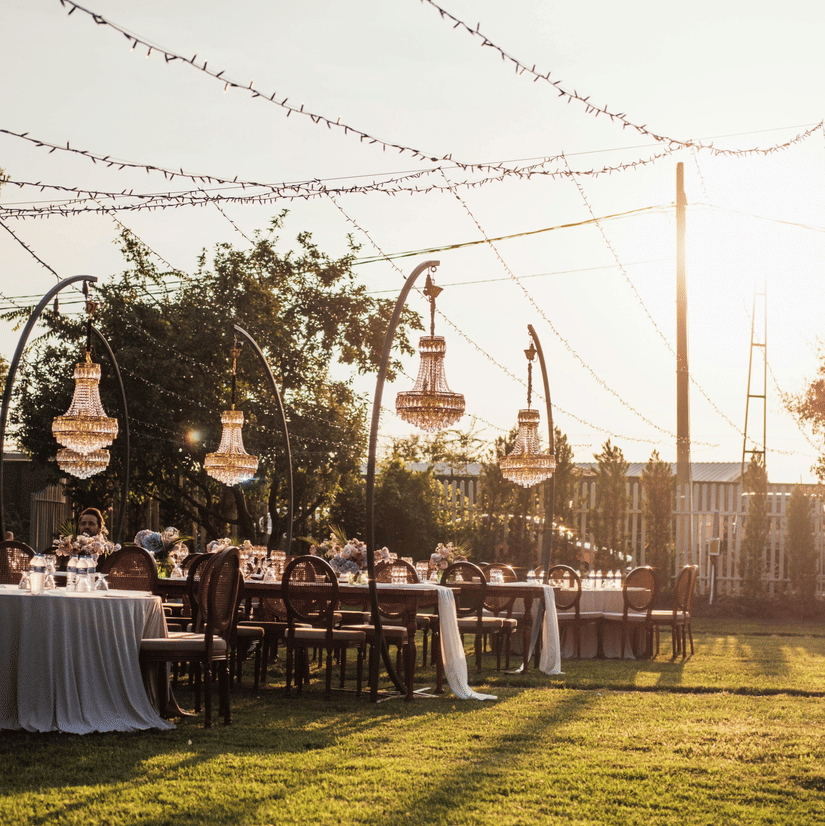 A garden area decorated for an event during the early evening hours with tables and chairs set.