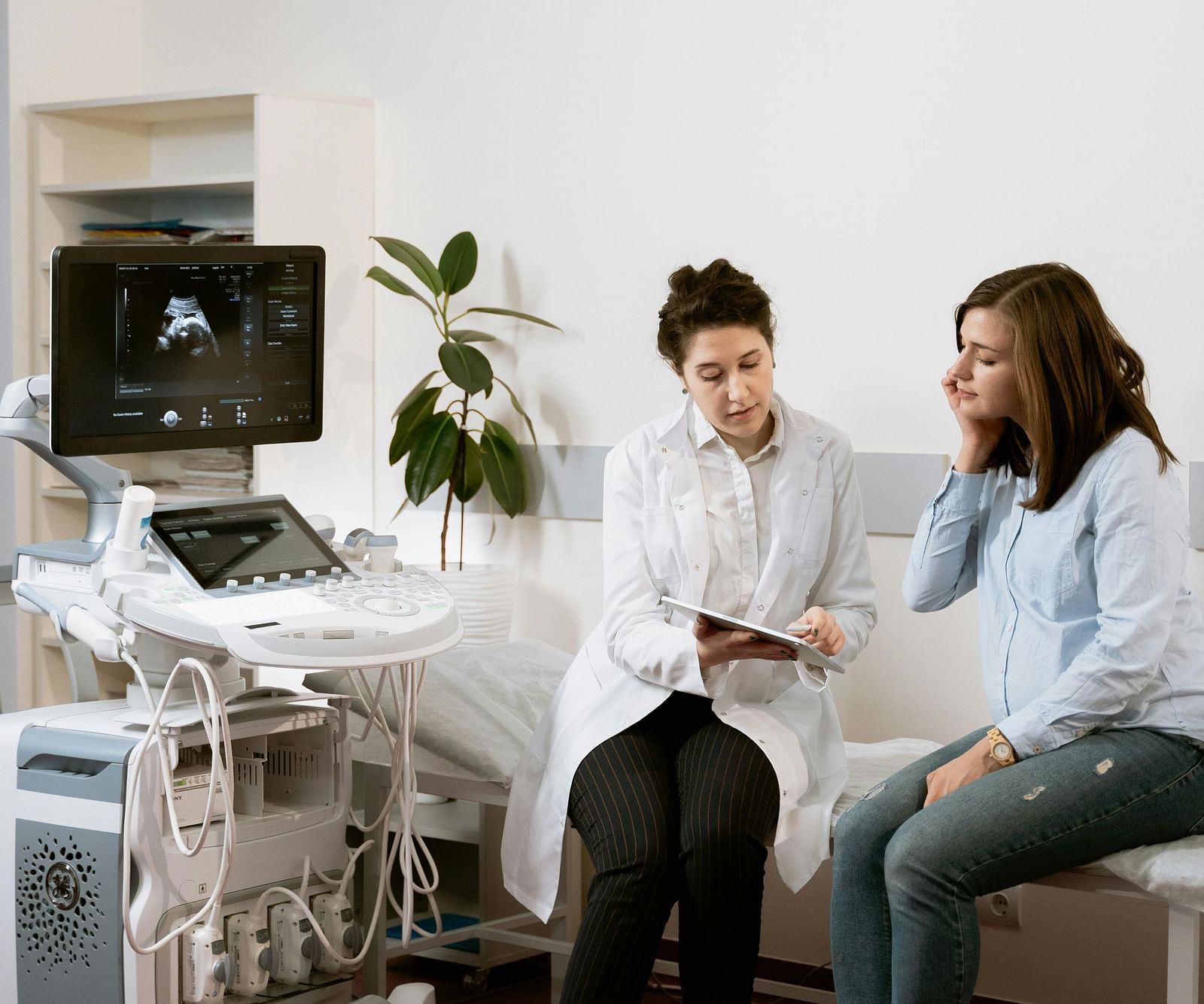 An image of doctor talking to a patient in a medical room which has various medical equipment