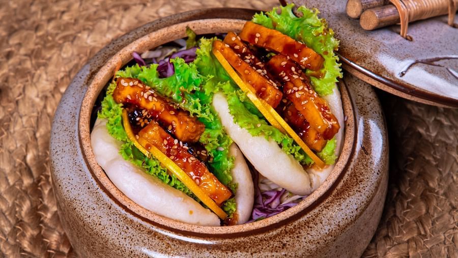 A bamboo steamer filled with buns stuffed with vibrant vegetables and proteins, accompanied by a tray of shredded purple cabbage and garnishes on a woven mat surface at The Hamuse Hotel, Kodaikanal.